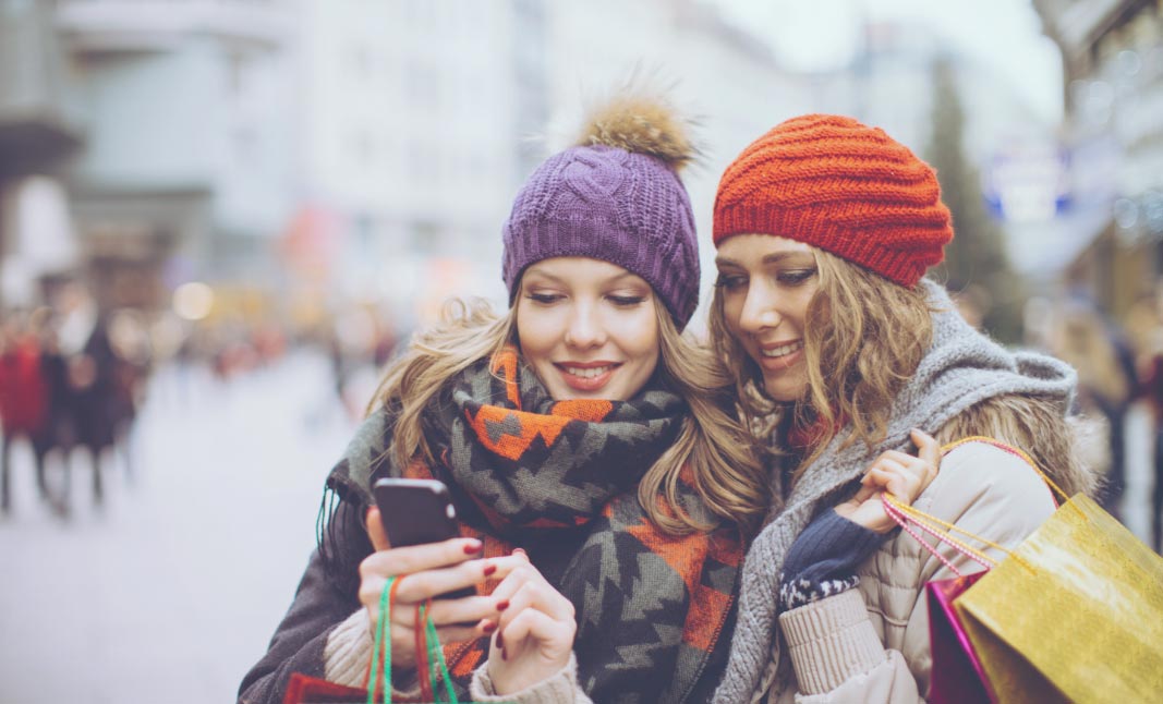 Two friends enjoying a shopping trip, one holds a phone and is showing the other an expense logged using expenditure.io